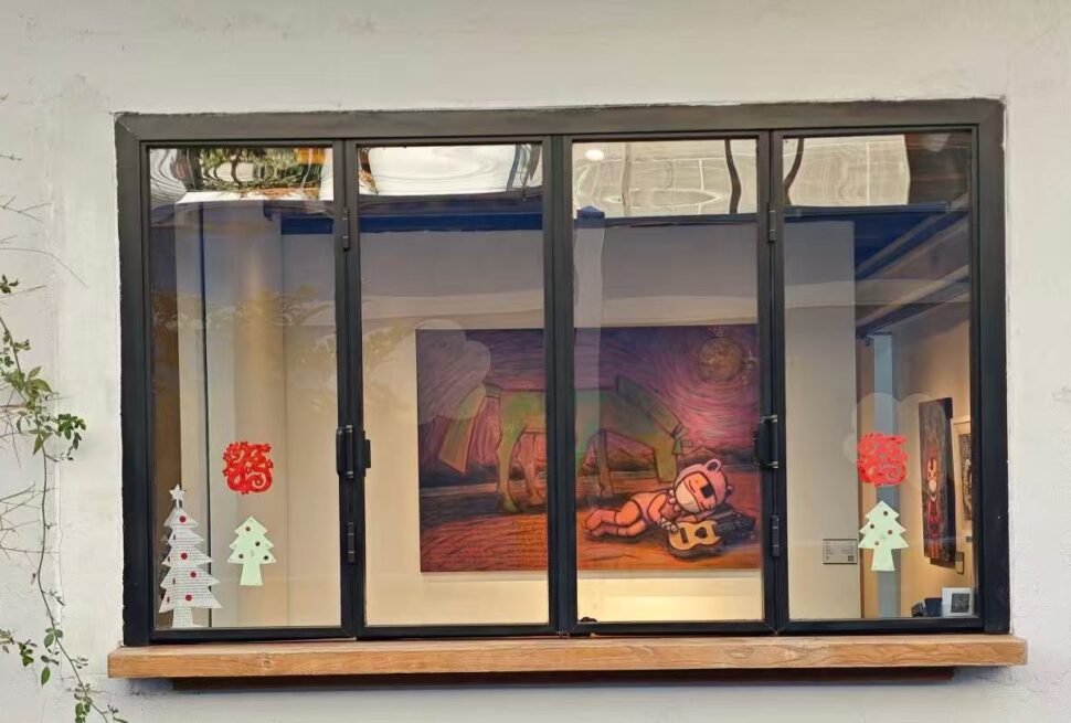 Shanghai M50 Creative Park ,Shanghai,Chinatour Storefront window with a black frame; inside is a colorful painting of a bear playing a guitar, flanked by holiday paper trees on the glass and red ornaments on the pane.