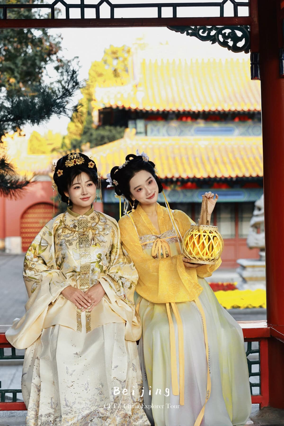 Hanfu photoshoot, the forbidden city, beijing, chinatravel, Two women in ornate traditional Chinese hanfu stand in a Beijing temple garden, one holding a woven lantern, with red columns and yellow tiled roofs in the background.