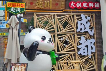 Front of a Chinese hotpot restaurant with a large panda statue holding a green cup, a bamboo lattice facade, and big white Chinese characters on the right.