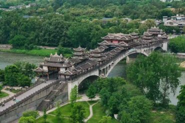 Huanglongxi Ancient Town,Chengdu,Chinatour Ornate multi-pavilion Chinese bridge spanning a river, surrounded by green trees and a hillside town in the background