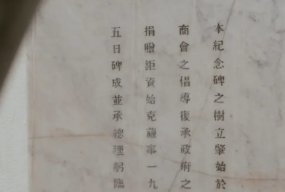 Stone marble memorial plaque with vertical Chinese text inscribed in neat columns, partially shadowed on the left.