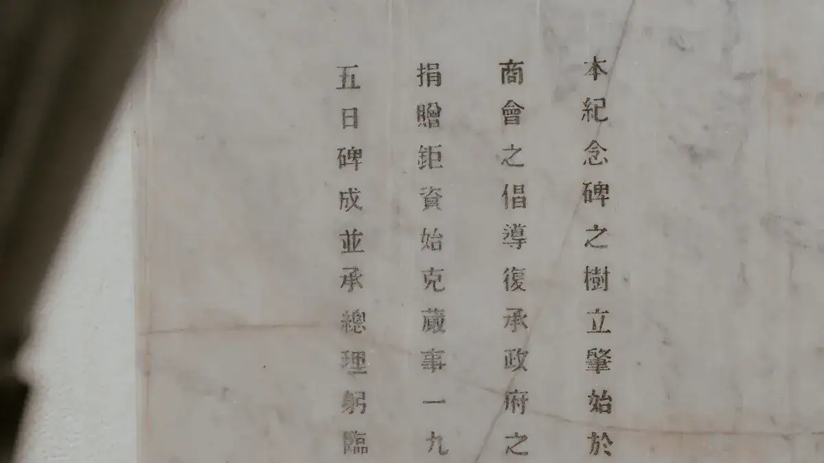 Stone marble memorial plaque with vertical Chinese text inscribed in neat columns, partially shadowed on the left.