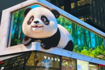 Giant panda mascot perched on a building billboard above a Volvo storefront in a city setting.