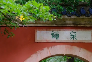 Wuhou Shrine,Chengdu,Chinatour White plaque with green Chinese characters 龍泉 on a red wall above a rounded arch, surrounded by green foliage.