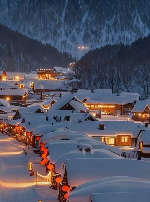 Snow-covered mountain village at night with warm lights glow from windows and street lamps along snow-filled streets.