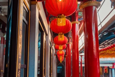 Temple corridor with bright red hanging lanterns and glossy red columns, gold accents, and ornate decorations.