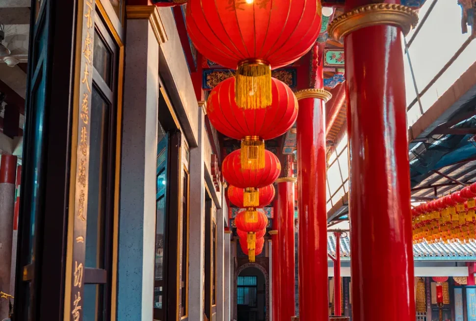 Temple corridor with bright red hanging lanterns and glossy red columns, gold accents, and ornate decorations.