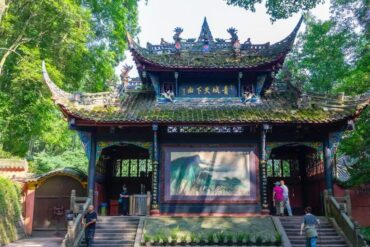 Mount Qingcheng and Dujiangyan,Chengdu,Chinatour Traditional Chinese pavilion tucked in a lush green garden with ornate roof dragons and a large landscape painting displayed inside the open hall, visitors examining the artwork.
