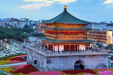 Bell and Drum Tower,Xi`an,Chinatour Traditional multi-tier Chinese pagoda atop a stone fortress overlooking a city, with colorful flowerbeds in the foreground.