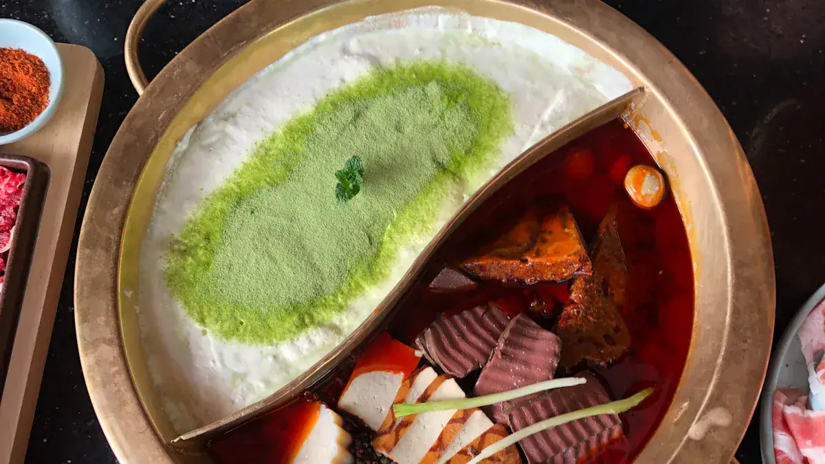 Split hot pot with milky white broth topped with green powder on the left and a red spicy broth with vegetables on the right.
