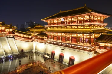 Tang Dynasty Show,Xi`an,Chinatour Nighttime view of a large illuminated Chinese palace complex with multi-tiered roofs and red walls, set in a spacious courtyard area.