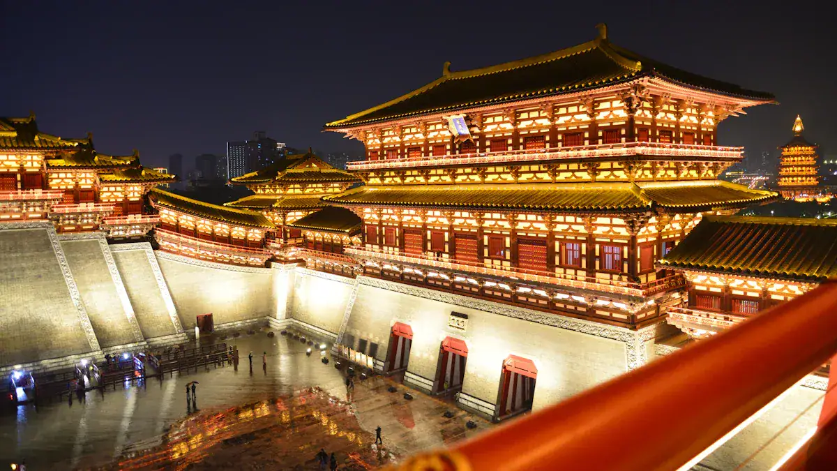 Nighttime view of a large illuminated Chinese palace complex with multi-tiered roofs and red walls, set in a spacious courtyard area.