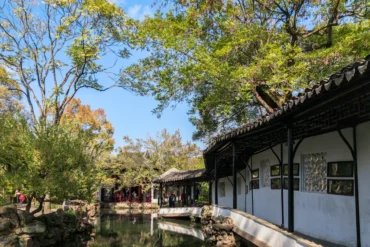 Humble Administrator's Garden,Suzhou,Chinatour Traditional Chinese garden with white-walled buildings, dark wooden beams, curved-tile roofs, and a reflecting pond.