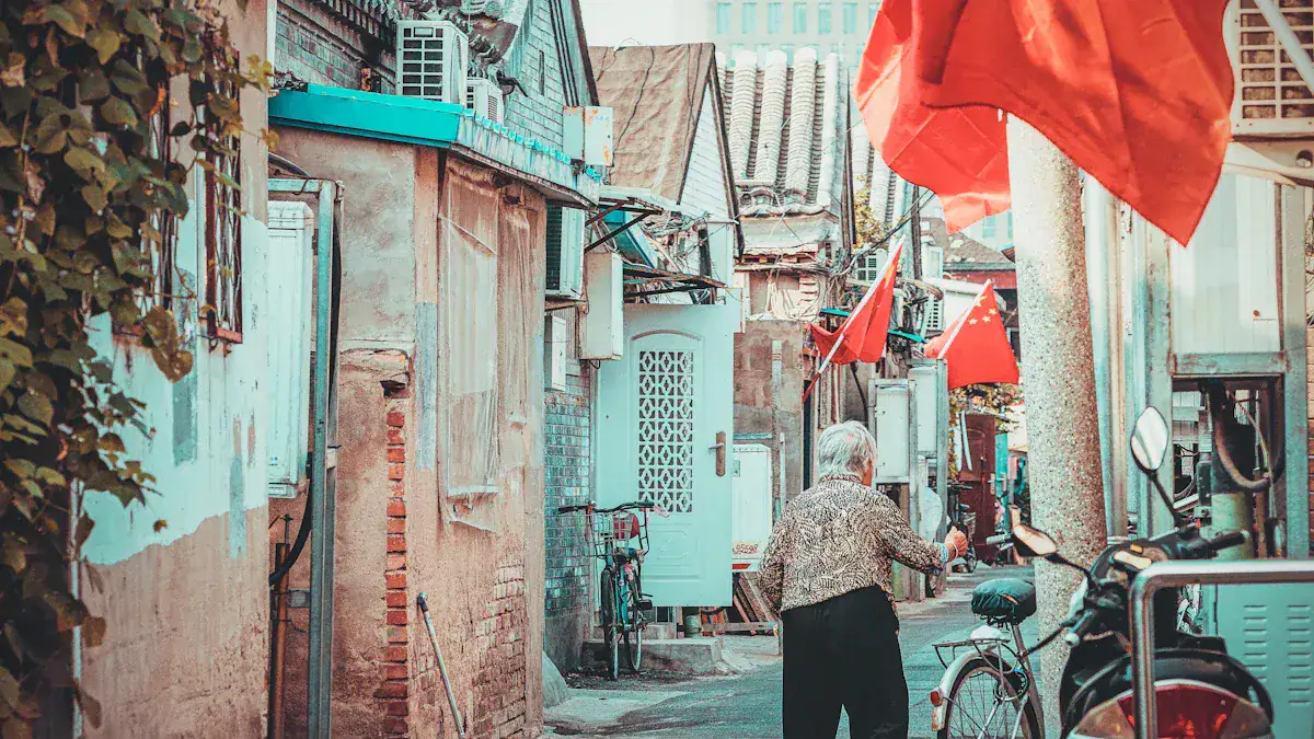 Older woman walks down a narrow alley between colorful old buildings with red Chinese flags overhead.