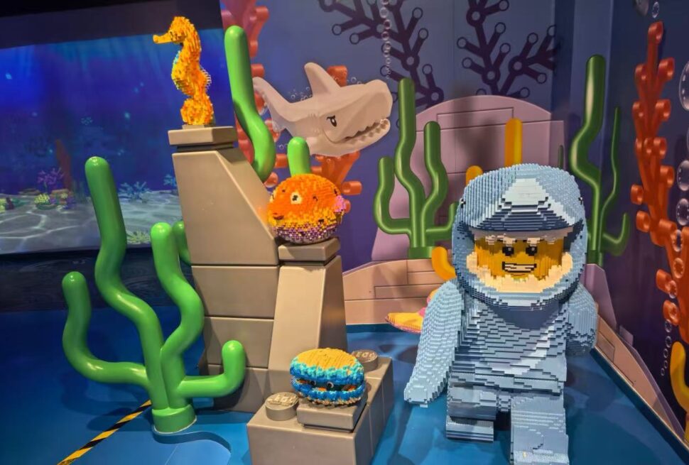 LEGO undersea display with a brick-built diver in blue, a white shark head, orange sea creatures, and green coral shapes.