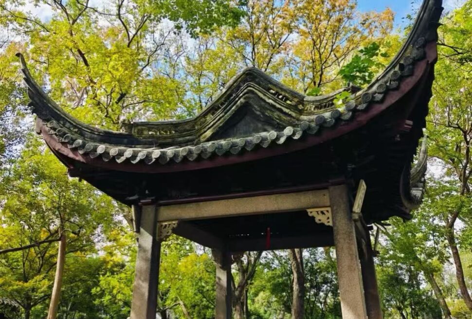 Traditional Chinese pavilion with curved tiled roof in a green garden setting under a blue sky