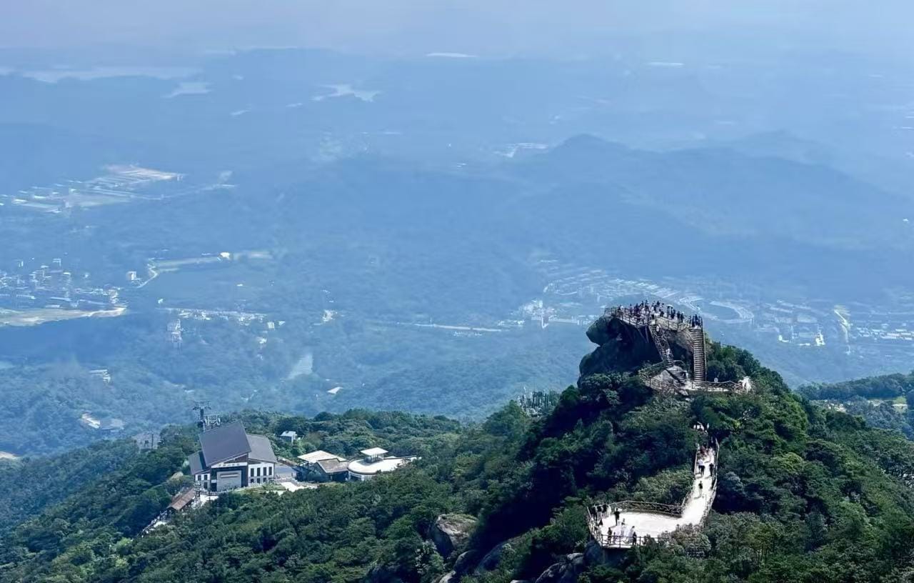 Luofu Mountain,Huizhou,Chinatour People stand on a crowded viewing platform at a rocky mountain peak, with a stairway winding up the trail.