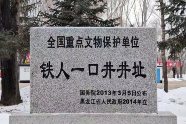 Granite stele with Chinese inscription declaring a national key cultural relic protection site, set in a snowy park with trees in the background.