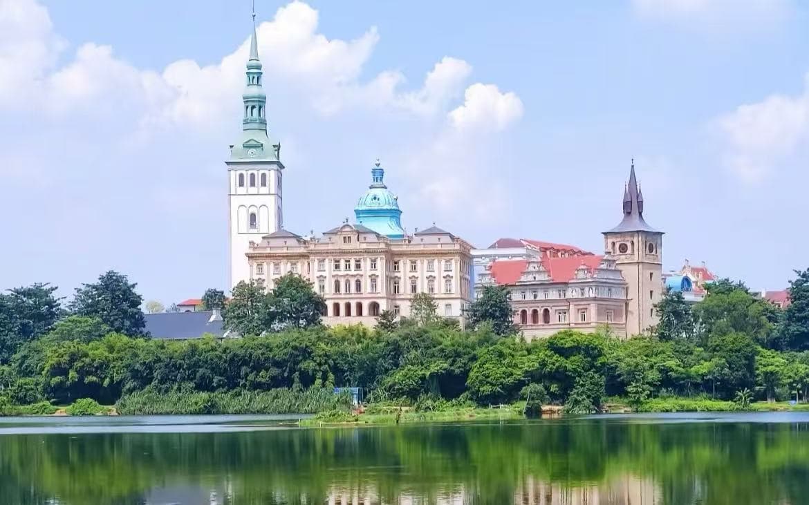 Songshan Lake,Dongguan,Chinatour European-style castle complex with tall spires by a tree-lined riverfront, reflection in the water