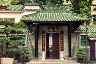 Traditional Chinese gate with a green tiled roof and red couplets, opening to a small courtyard garden.