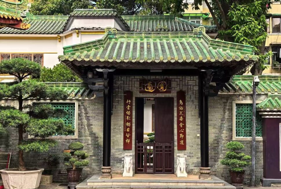 Temple of the Six Banyan Trees,Guangzhou,Chinatour Traditional Chinese gate with a green tiled roof and red couplets, opening to a small courtyard garden.