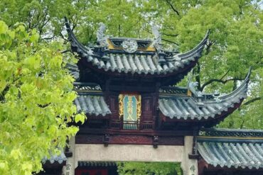 Xiyuan Temple,Suzhou,Chinatour Traditional Chinese temple gate with curved eaves and ornate roof, green signboard with gold characters, surrounded by trees.