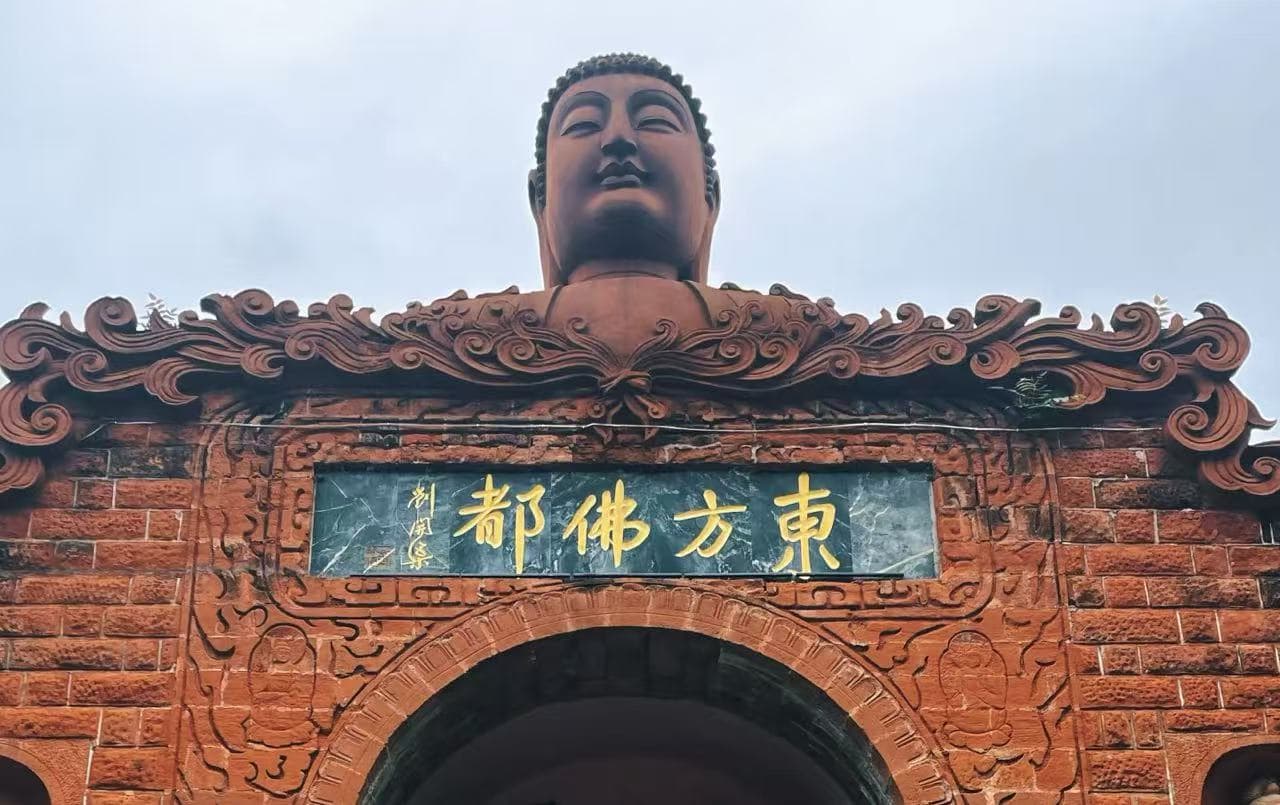 Buddha head statue perched above an ornate red brick gateway with gold Chinese inscription plaque.