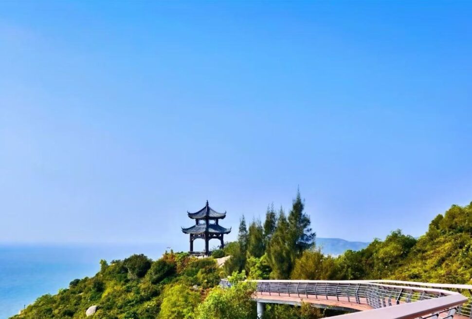 Traditional pagoda on a hillside overlooking a blue sea, with a curved wooden boardwalk in the foreground.