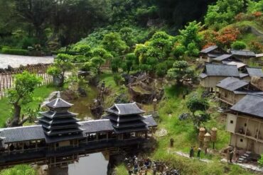 Miniature traditional Asian village with tiered pagoda buildings, a wooden bridge, and lush garden scenery.