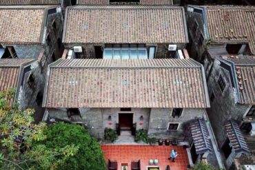 Xiguan Ancient Mansion,Guangzhou,Chinatour Aerial view of grey brick houses with tiled roofs forming a narrow courtyard, red tile courtyard in front of a central doorway with a person nearby.