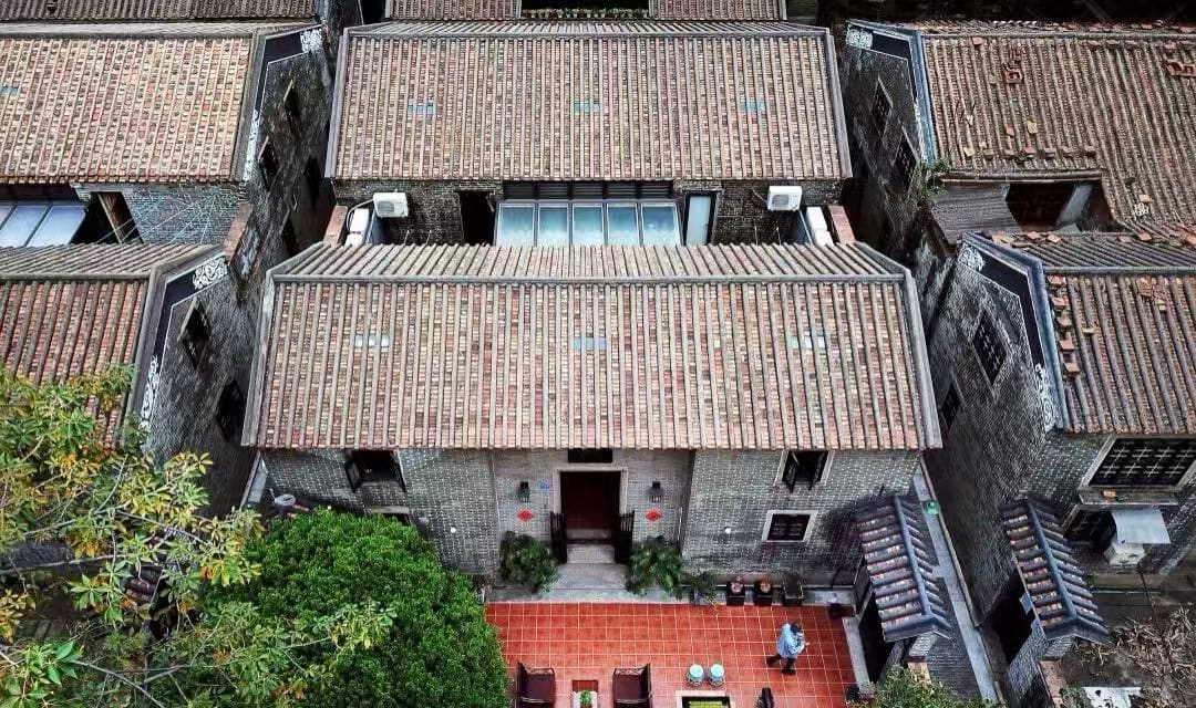 Aerial view of grey brick houses with tiled roofs forming a narrow courtyard, red tile courtyard in front of a central doorway with a person nearby.