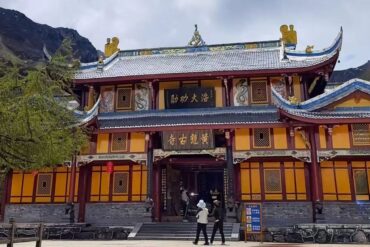 Front view of a colorful traditional Chinese temple with ornate roof decorations and yellow walls, set against rocky mountains. (Informative)