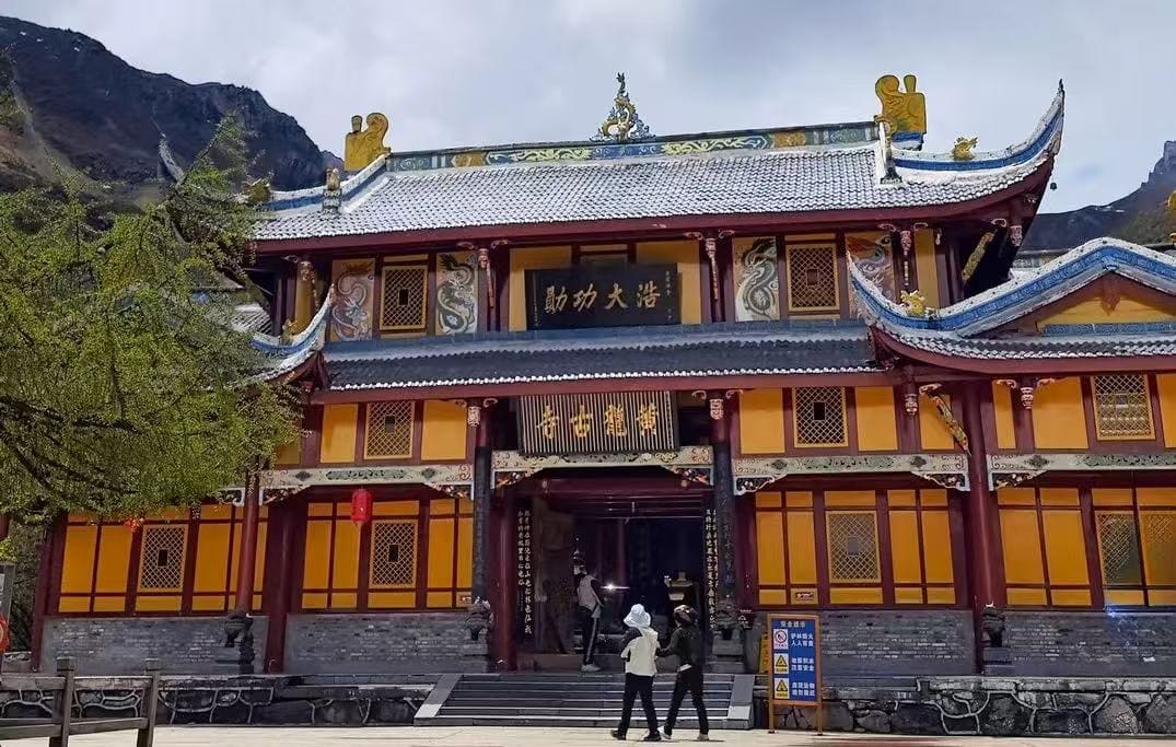 Huanglong Temple,Western Sichuan,Chinatour Front view of a colorful traditional Chinese temple with ornate roof decorations and yellow walls, set against rocky mountains. (Informative)