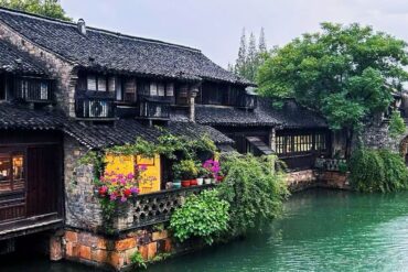 Wuzhen Water Town ,Hangzhou,Chinatour Canal-side stone houses with tiled roofs and hanging balconies, colorful flowers in pots along the wall.