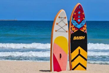 Dadonghai Beach,Sanya,Chinatour Two colorful surfboards upright in the sand at the beach with blue ocean and waves behind them.