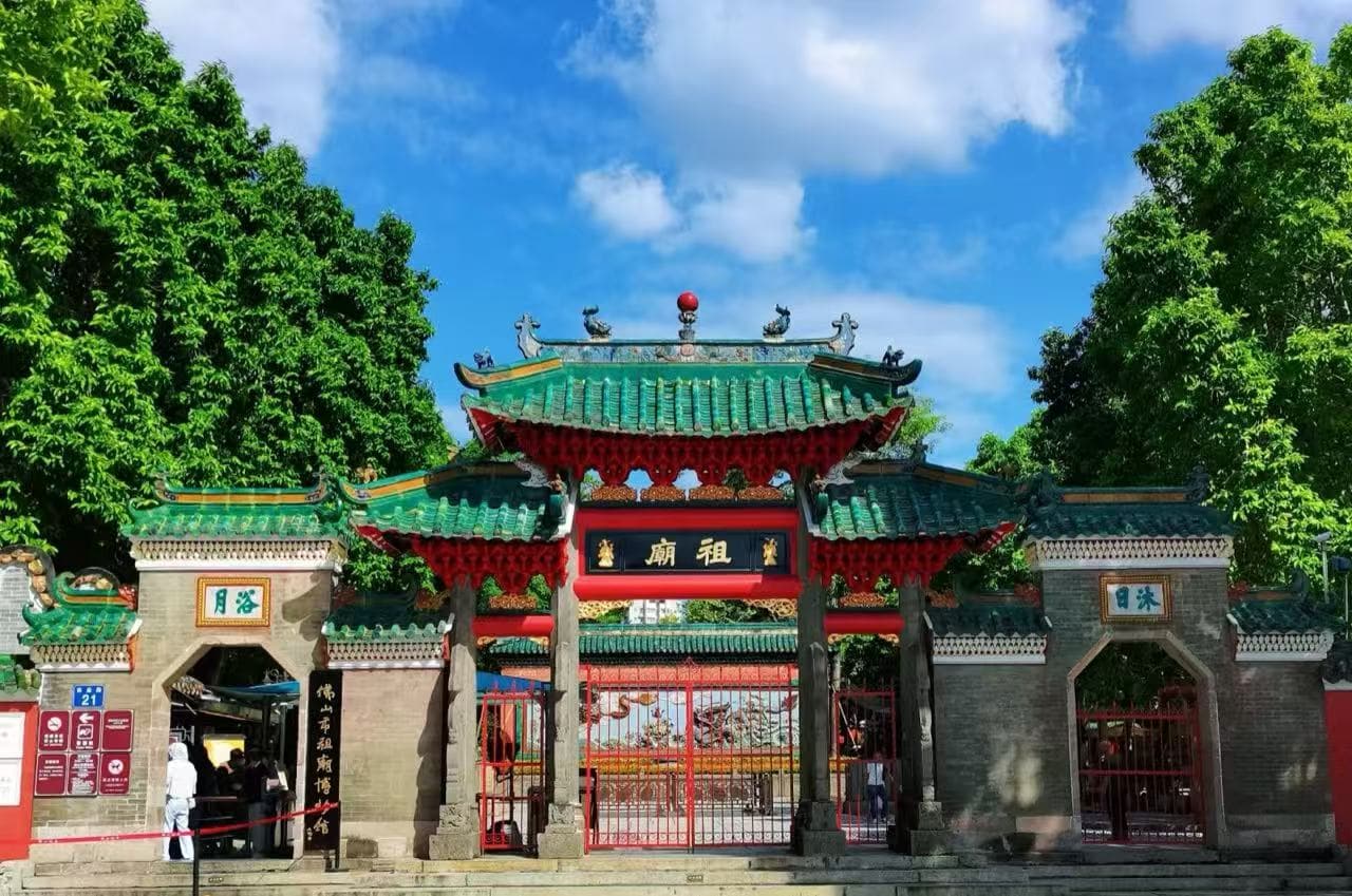 Ancestral Temple ,Guangzhou,Chinatour Traditional Chinese temple gate with a green tiled roof, red pillars, and ornate Details, set between lush trees under a blue sky.