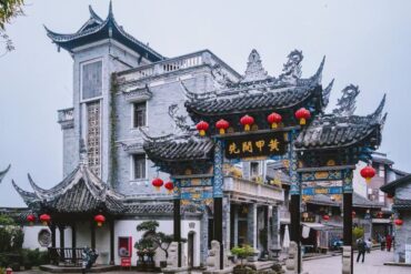 Tongliang Ancient Town,Chongqing,Chinatour Ornate Chinese paifang arch with blue-gold detailing and red lanterns in a temple courtyard
