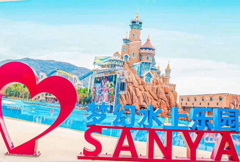 Sanya Fantasy Water World,Sanya,Chinatour A bright water park entrance with a large pink heart sculpture and blue sign reading 梦幻水上乐园 SANYA against a castle backdrop.