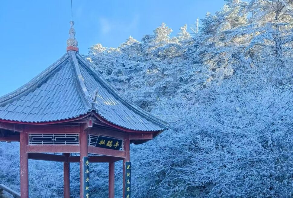 Mount Emei Scenic Area,Leshan,Chinatour Red Chinese pavilion with a blue tiled roof in a snow-covered forest under a clear blue sky.
