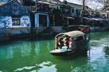 Xitang Water Town,Hangzhou,Chinatour Tour boat with a woven canopy glides along a green canal beside blue-washed houses adorned with red lanterns. Family passengers sit inside the boat.