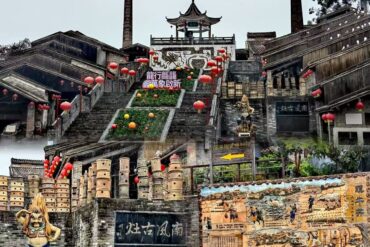 Tiered stone steps lined with red lanterns leading up to a traditional Chinese pavilion atop a temple complex.