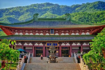 Nanshan Temple & Giant Guanyin Statue,Sanya,Chinatour Temple with red and green tiled roof, stone stairs, and a bronze incense burner, set against a forested hillside.