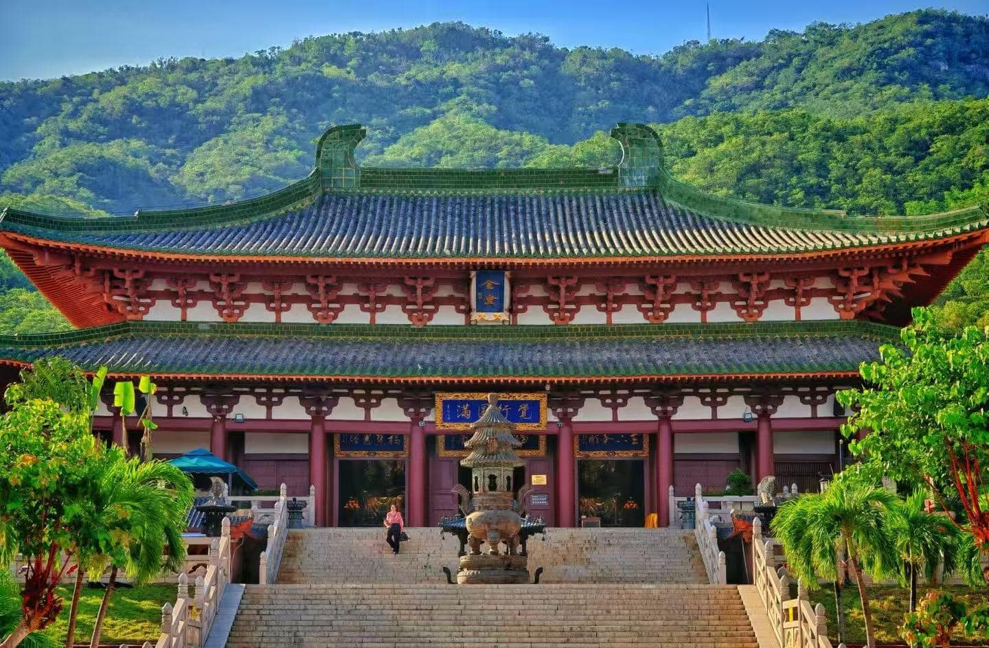 Nanshan Temple & Giant Guanyin Statue,Sanya,Chinatour Temple with red and green tiled roof, stone stairs, and a bronze incense burner, set against a forested hillside.