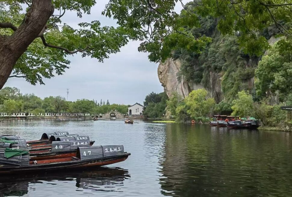 East Lake,Shaoxing,Chinatour Rowboats numbered 40–47 docked along a calm river with green trees and a rocky cliff in the background.