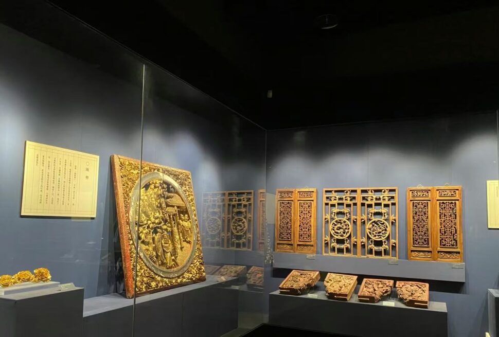 Ornate gilded wooden panels and carved plaques on display in a museum case against a dark wall.