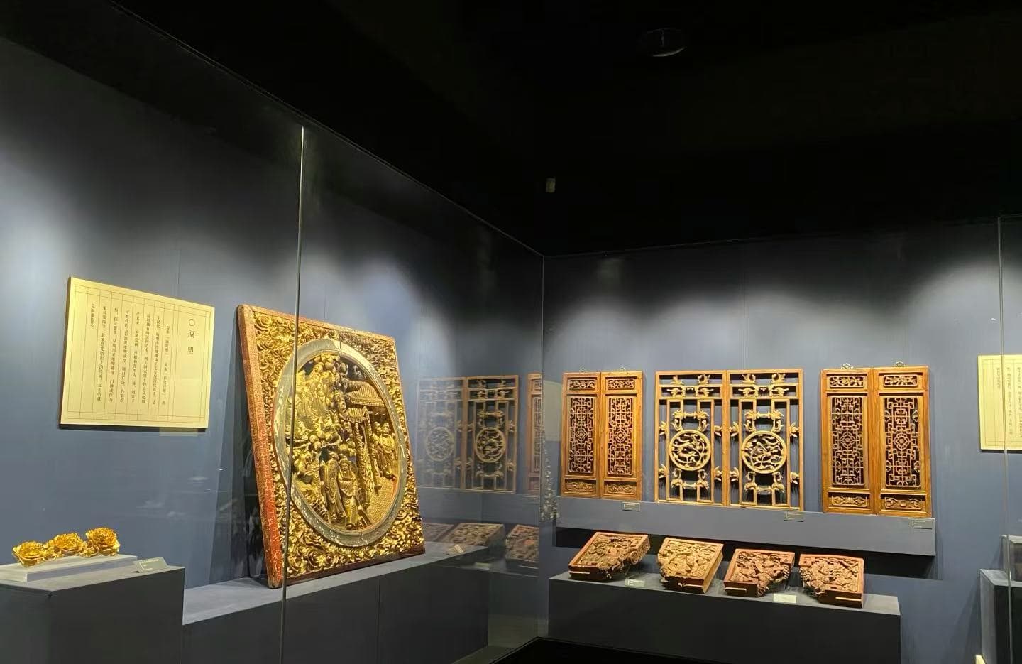 Wenzhou Museum ,Wenzhou,Chinatour Ornate gilded wooden panels and carved plaques on display in a museum case against a dark wall.