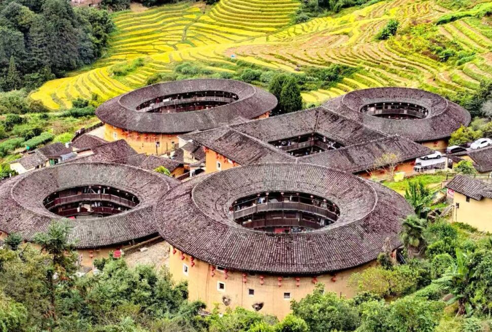 Tianluokeng Tulou Cluster,Zhangzhou,Chinatour Cluster of round tulou earth buildings with inner courtyards in a hillside village; terraced fields in the background, lush greenery surrounding.