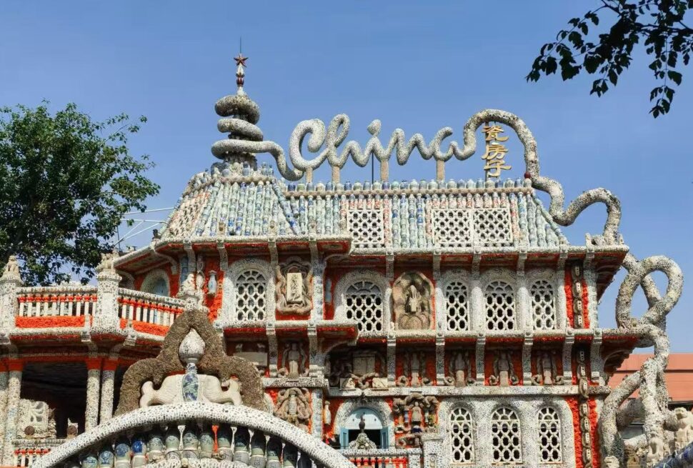 China House,Tianjin,Chinatour Elaborately decorated mosaic building with curved, organic shapes, stone lattice windows, and a large cursive sign on the roof against a blue sky.