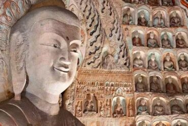 Yungang Grottoes,Datong,Chinatour Giant carved Buddha statue inside a cave temple, with hundreds of smaller Buddha figures in niches along the wall.