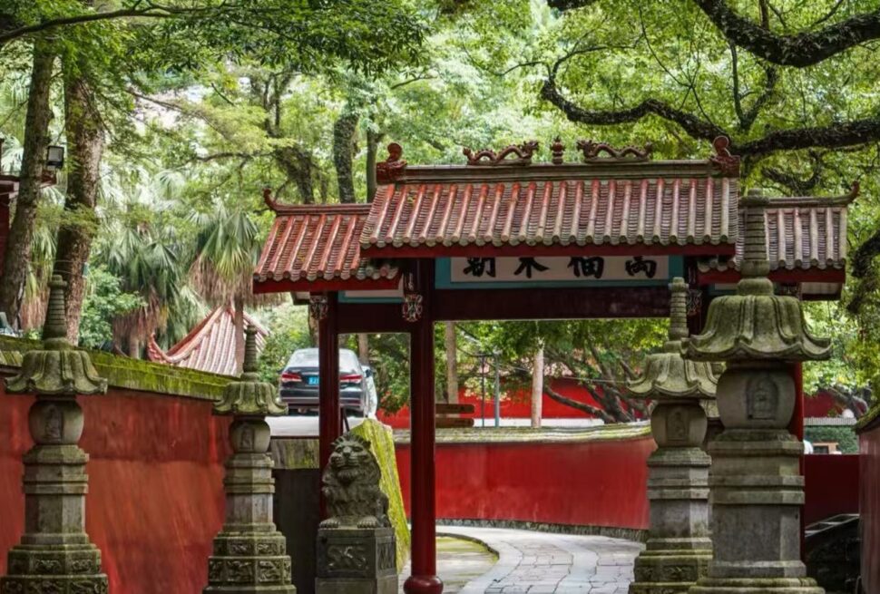 Yongquan Temple,Fuzhou,Chinatour Traditional Chinese temple gate with red tiled roof, stone lanterns, and a curved stone path surrounded by lush greenery.